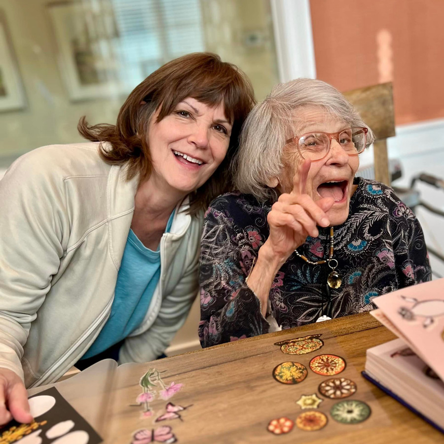 Senior resident and staff member happily enjoying a creative activity together, with colorful designs and stickers spread across the table, sharing a joyful moment at a senior living community.