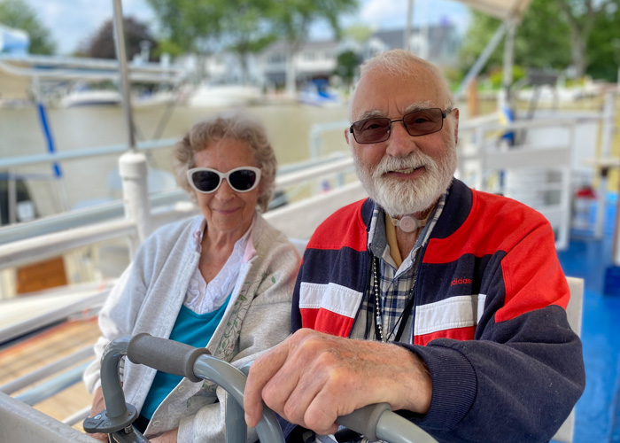 Two smiling seniors enjoying a boat ride, showcasing their sense of adventure and the active lifestyle available in senior living communities, with a serene marina in the background.